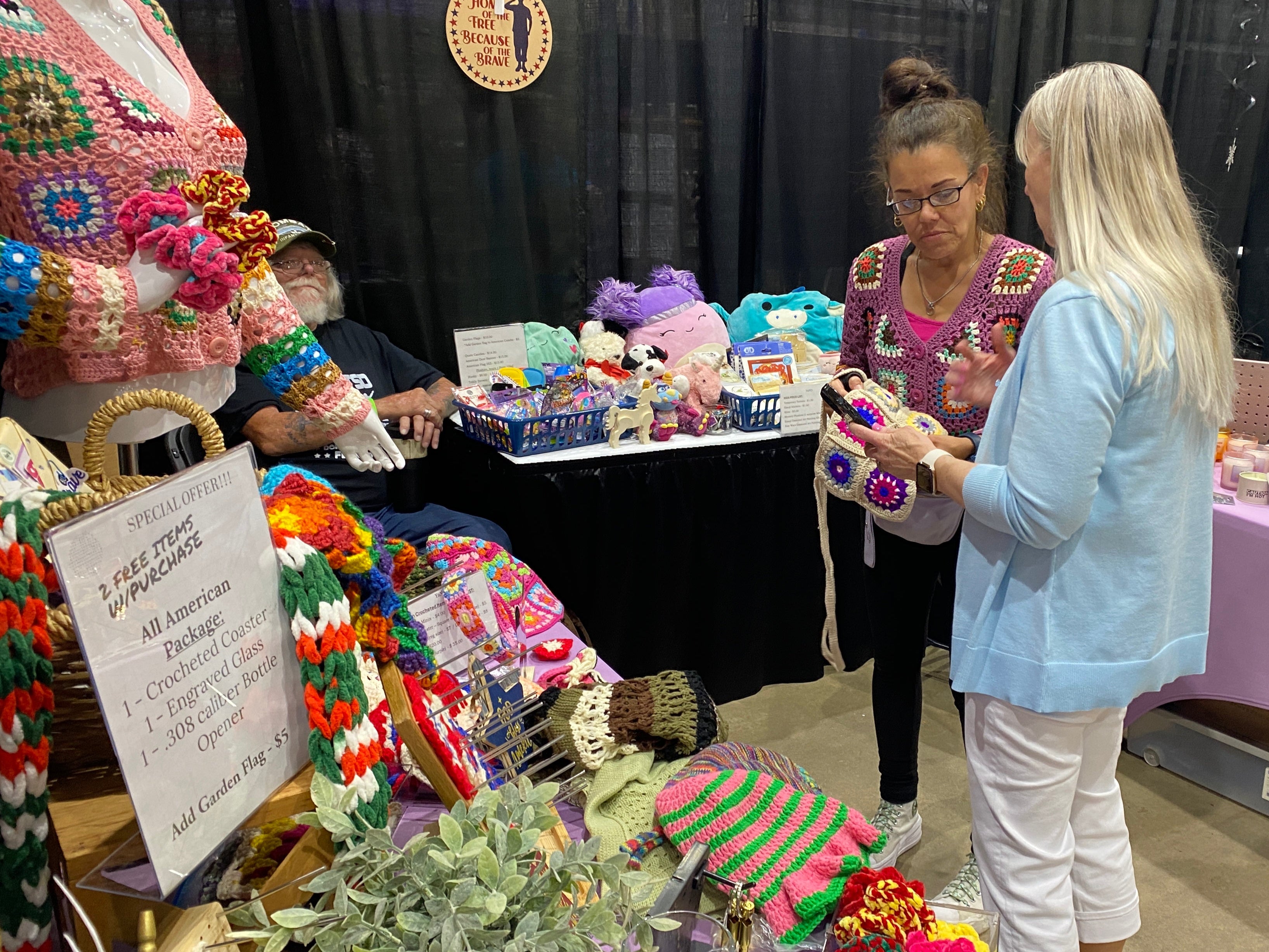 Two women at a craft show booth with various handmade items on display.